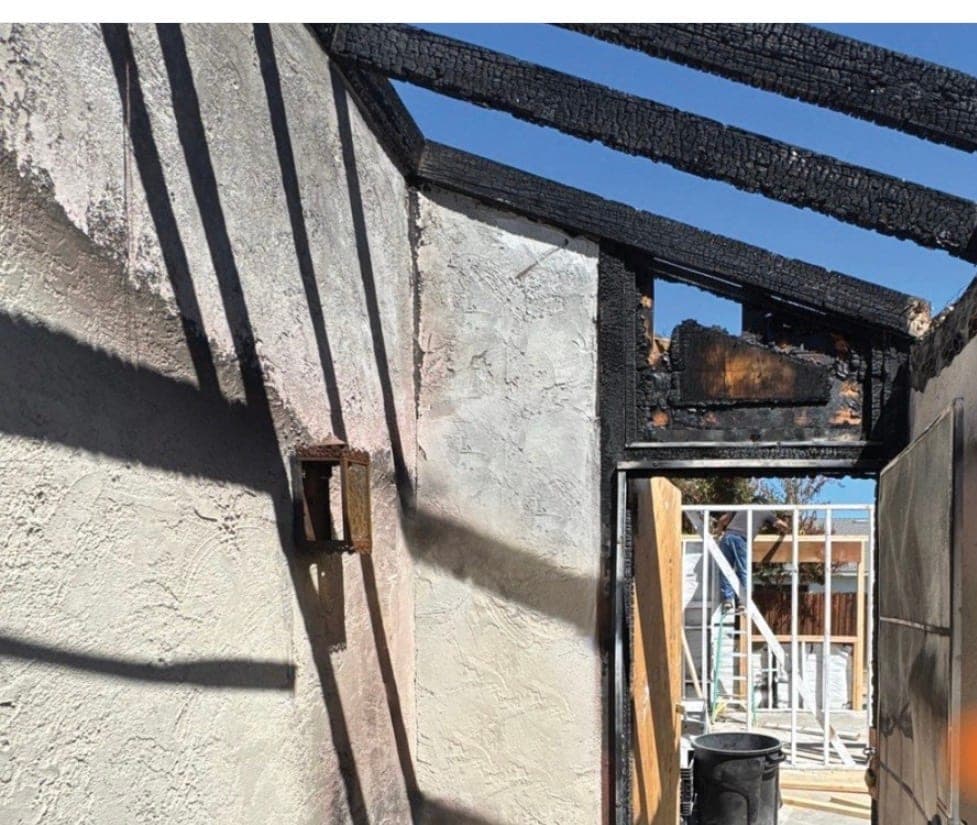 Charred beams and smoke-stained stucco at the entry of a fire-damaged house, before reconstruction