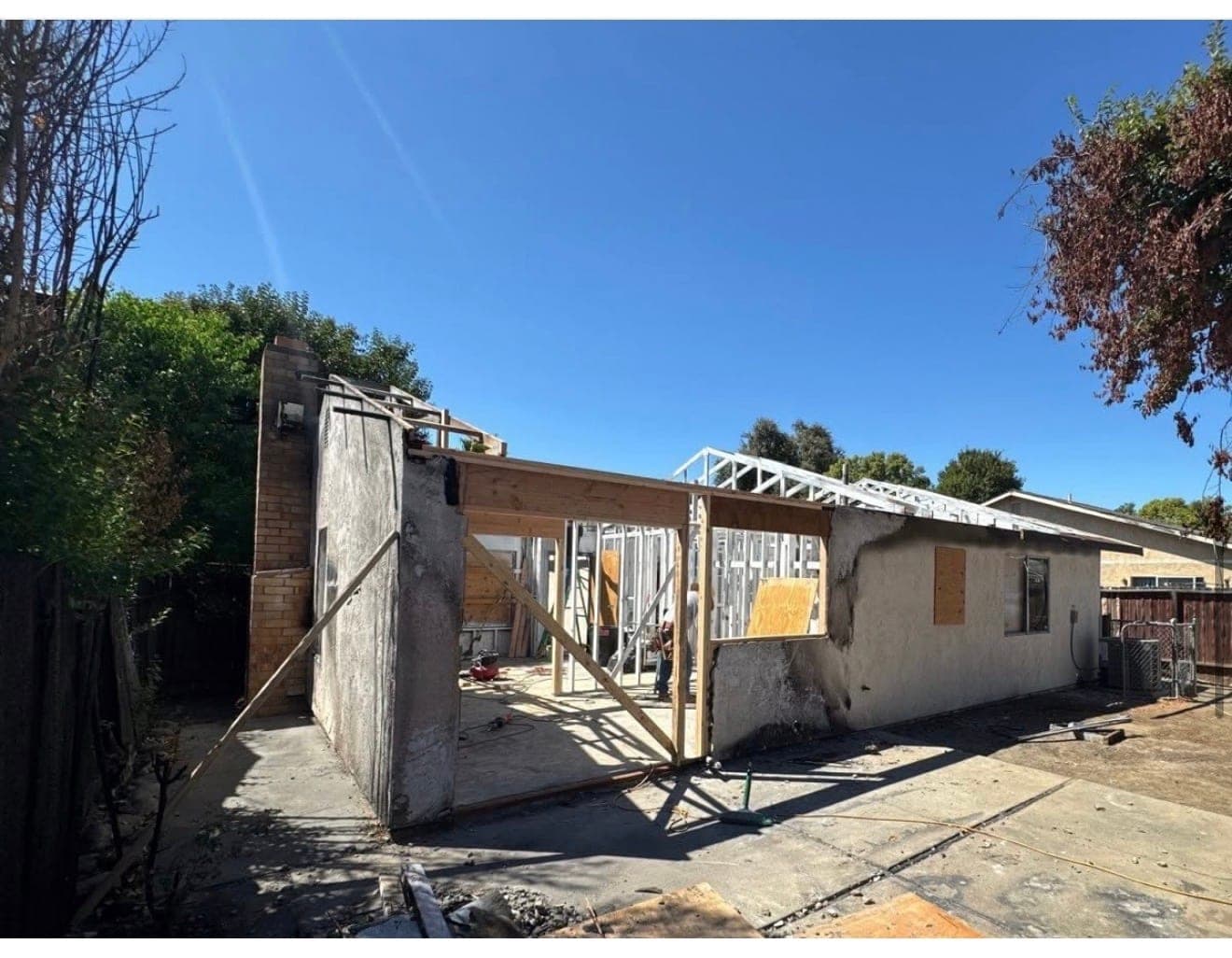 Exterior of a fire-damaged single-family house being reframed, with new roof trusses set against a clear sky