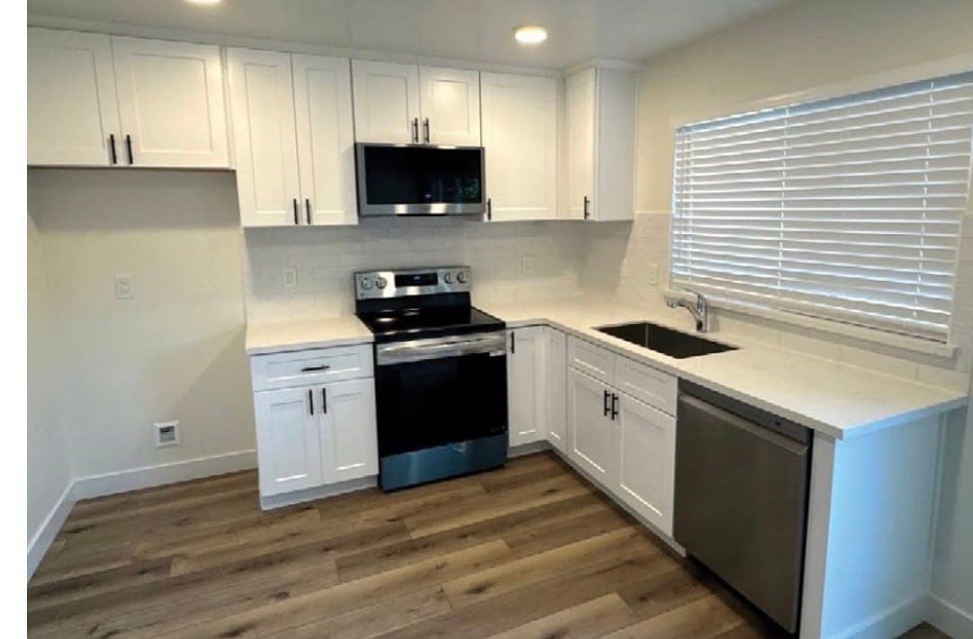 The finished kitchen: white shaker cabinets, quartz counters, tile backsplash, stainless appliances and new plank flooring